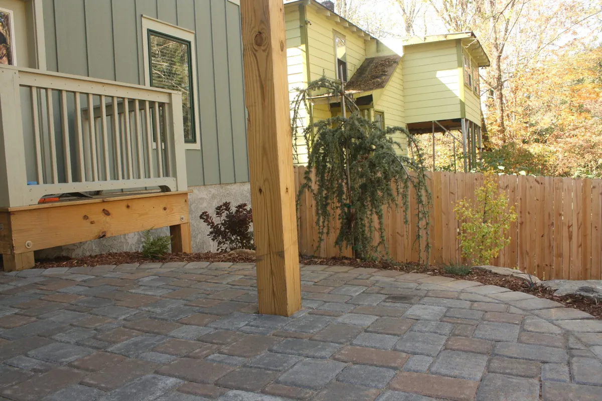 Backyard interlocking concrete paver patio with curved edges, under deck space, and surrounding planting beds