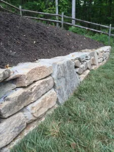 Natural stone retaining wall built into a sloped yard with soil backfill and lawn edging